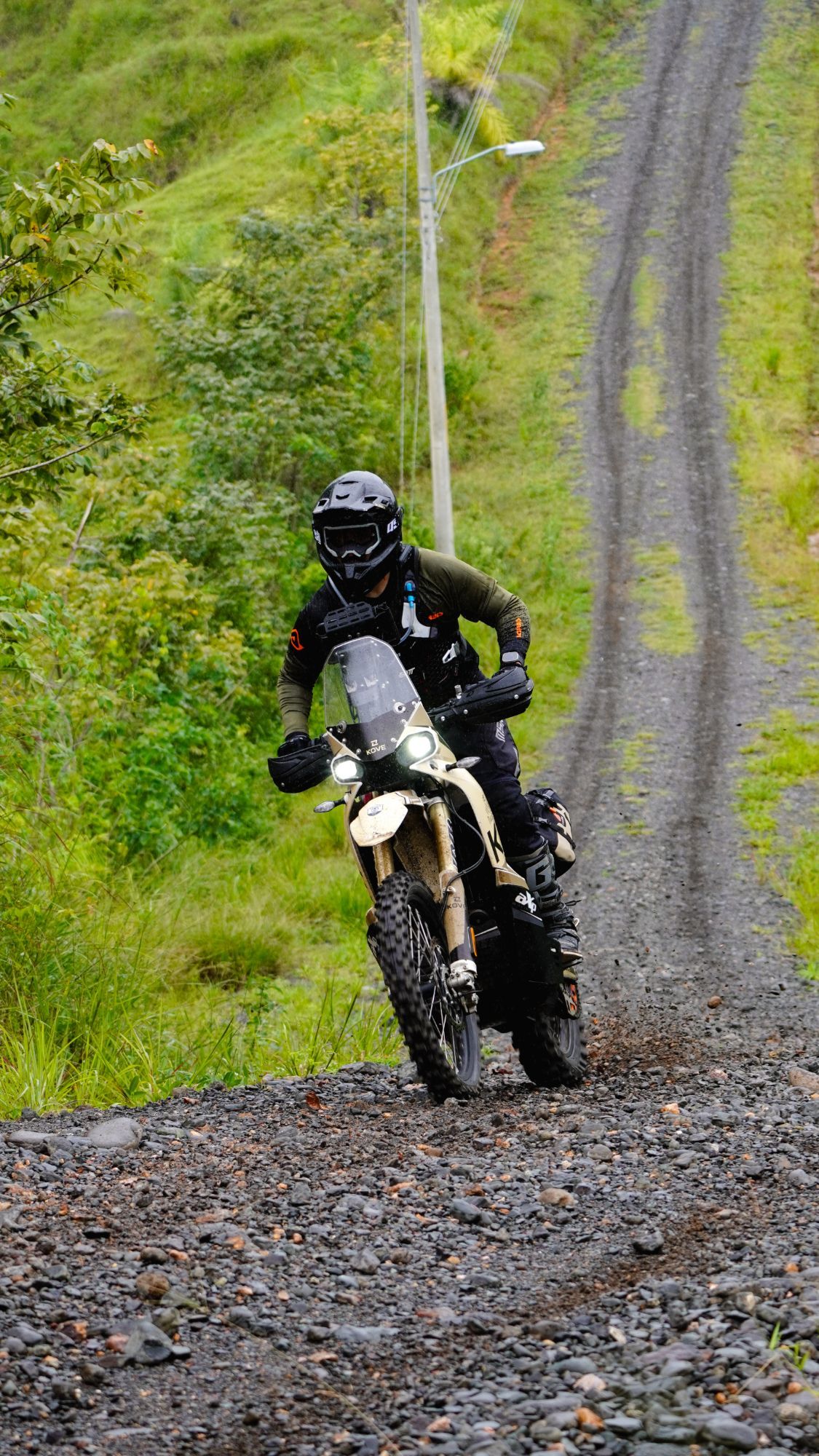 Motociclista subiendo un camino de lastre en una Kove, con las luces encendidas.