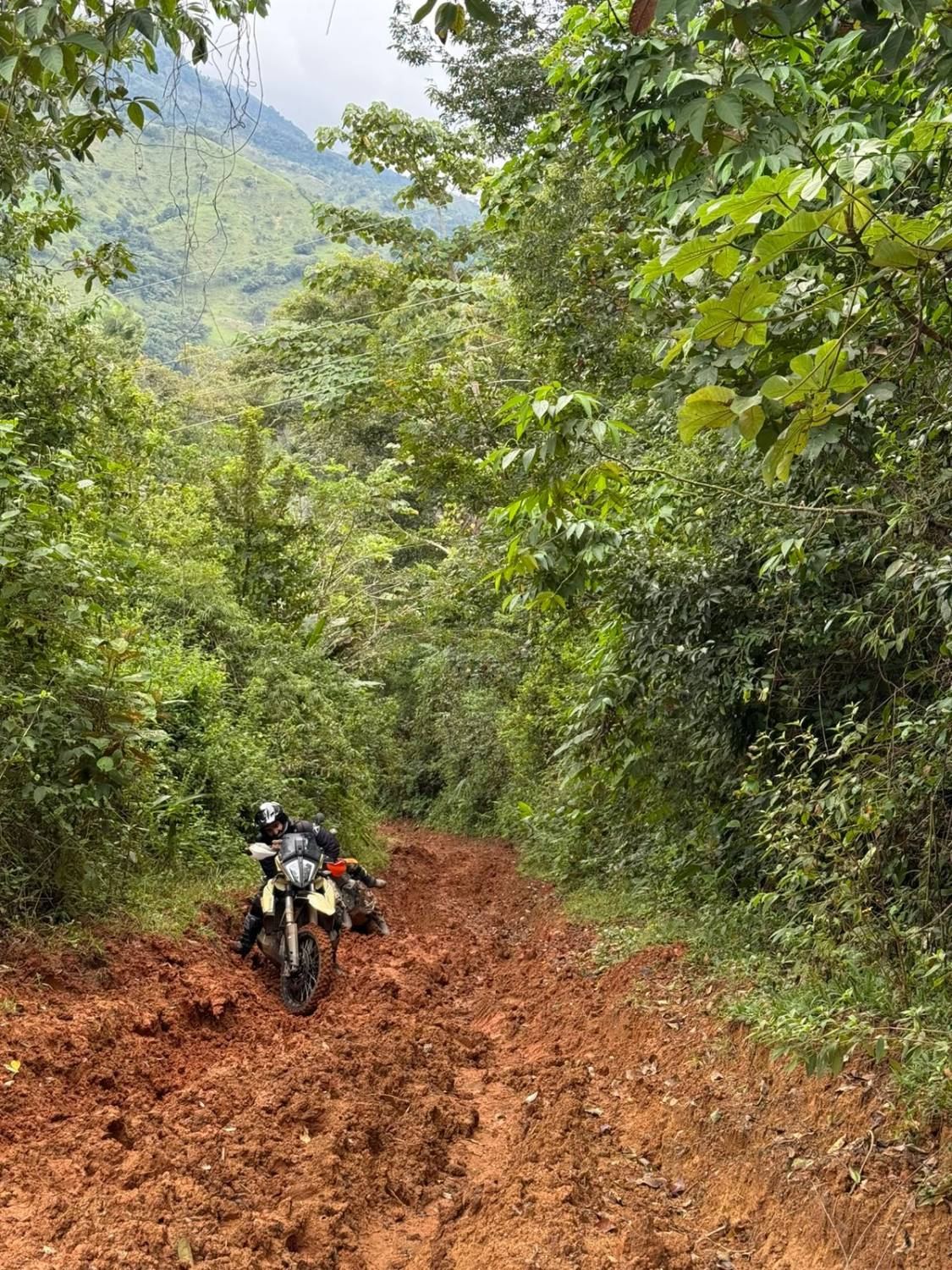 Motociclista abriéndose paso por un trillo de barro rojo en medio de la montaña.